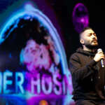 Tamer Hosny performing on stage during a Christmas event, captivating the audience with his music amidst festive decorations and lights.