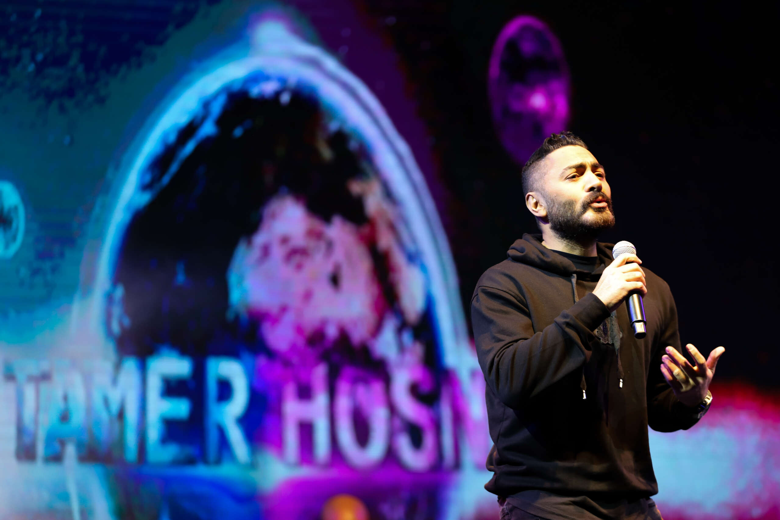 Tamer Hosny performing on stage during a Christmas event, captivating the audience with his music amidst festive decorations and lights.