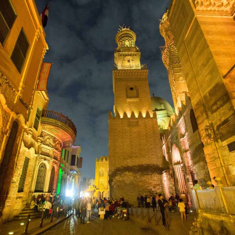 A view of Al-Muizz Street in Cairo at night, with its historic mosques beautifully illuminated, showcasing the stunning architecture and vibrant lights.