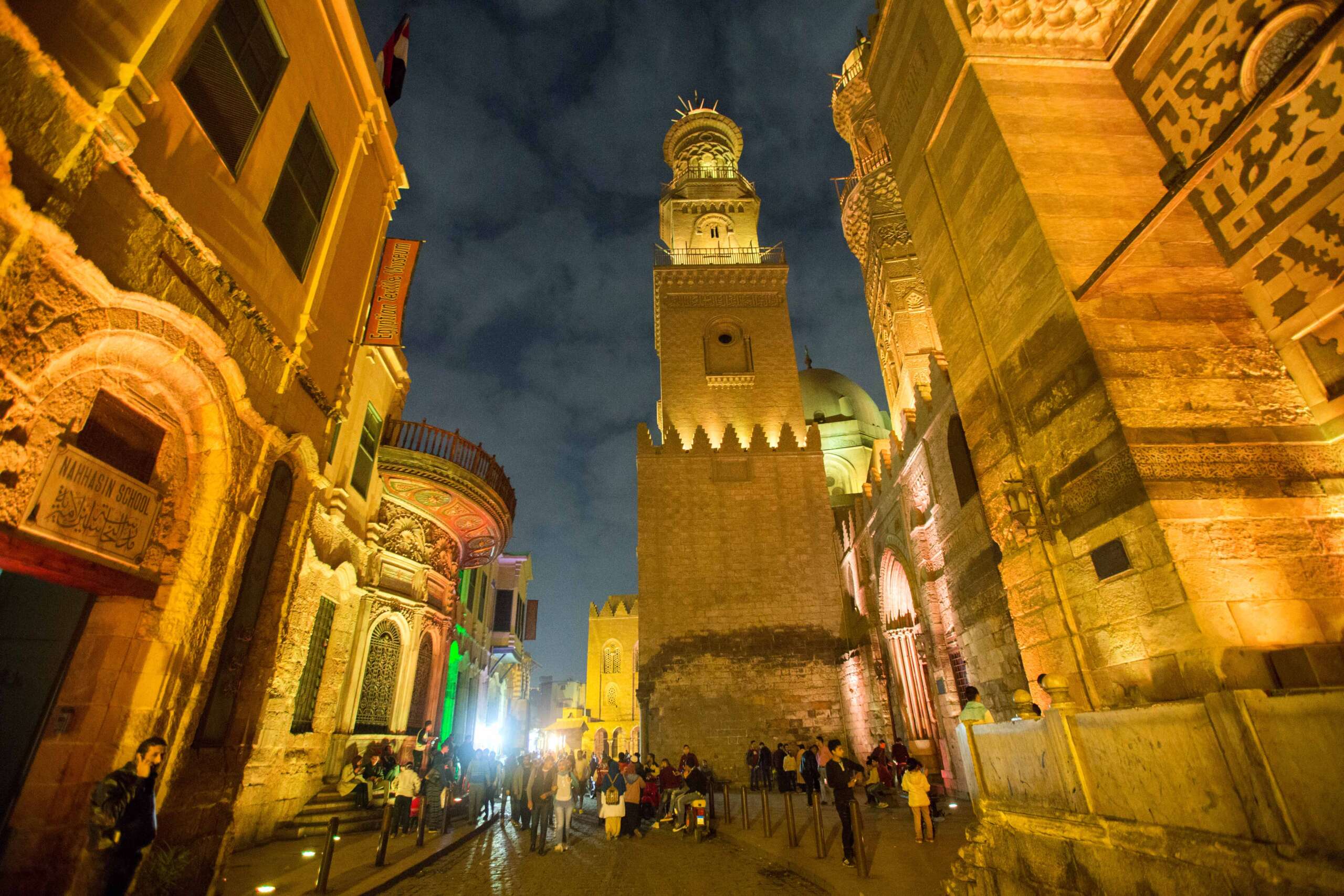 A view of Al-Muizz Street in Cairo at night, with its historic mosques beautifully illuminated, showcasing the stunning architecture and vibrant lights.