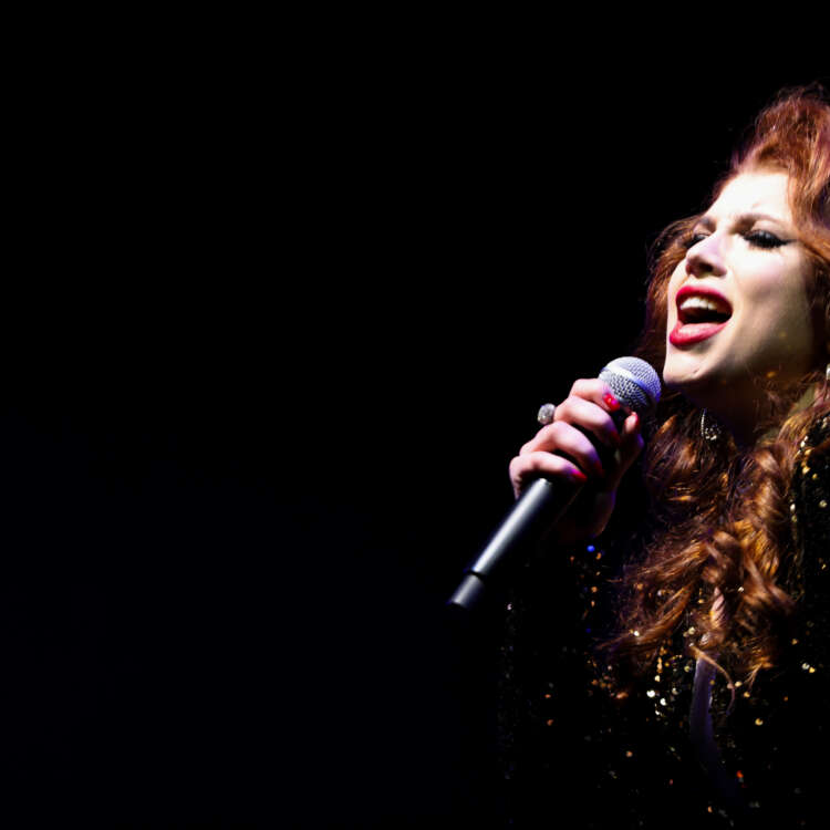 A girl singing in front of a Christmas tree adorned with lights and decorations, creating a festive holiday atmosphere.