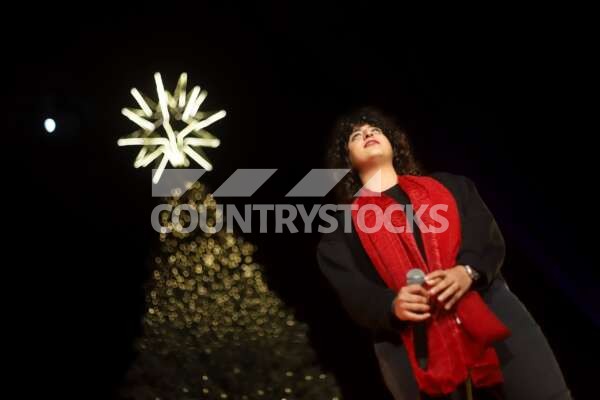 A girl singing in front of a Christmas tree adorned with lights and decorations, creating a festive holiday atmosphere.