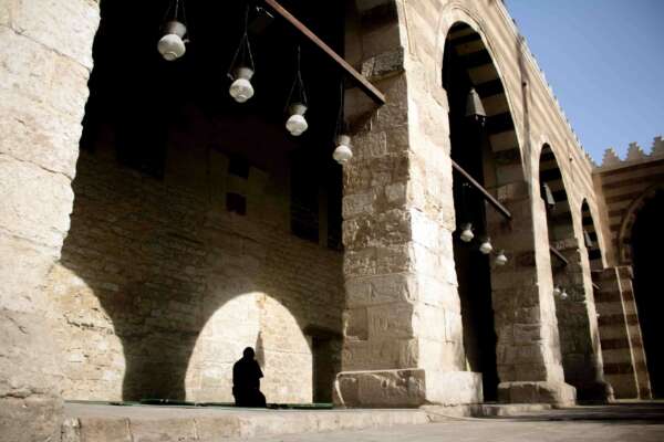 A man praying inside the Blue Mosque in Old Cairo, surrounded by the mosque's intricate architecture and serene atmosphere.