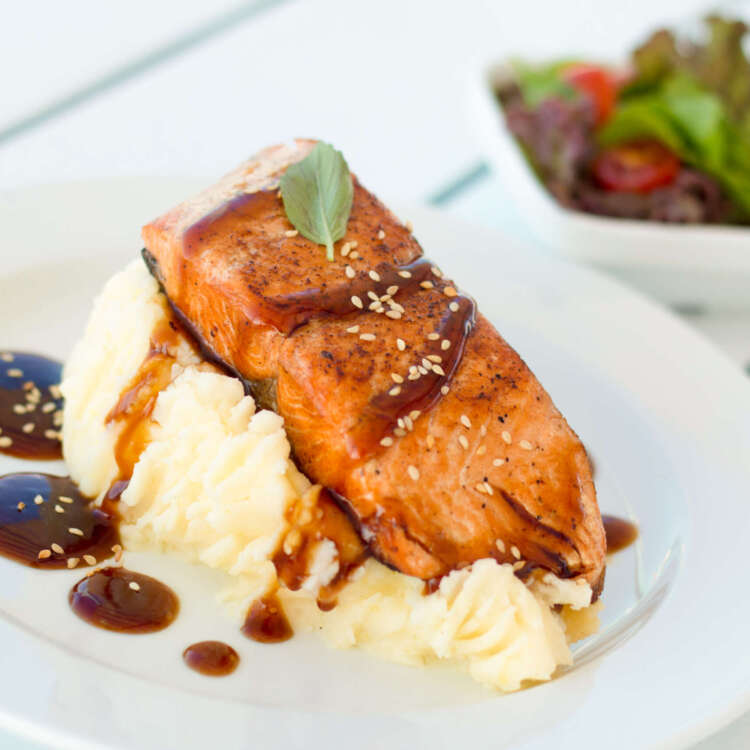 A plate featuring a fresh slice of salmon served alongside creamy mashed potatoes, garnished with herbs for an elegant meal