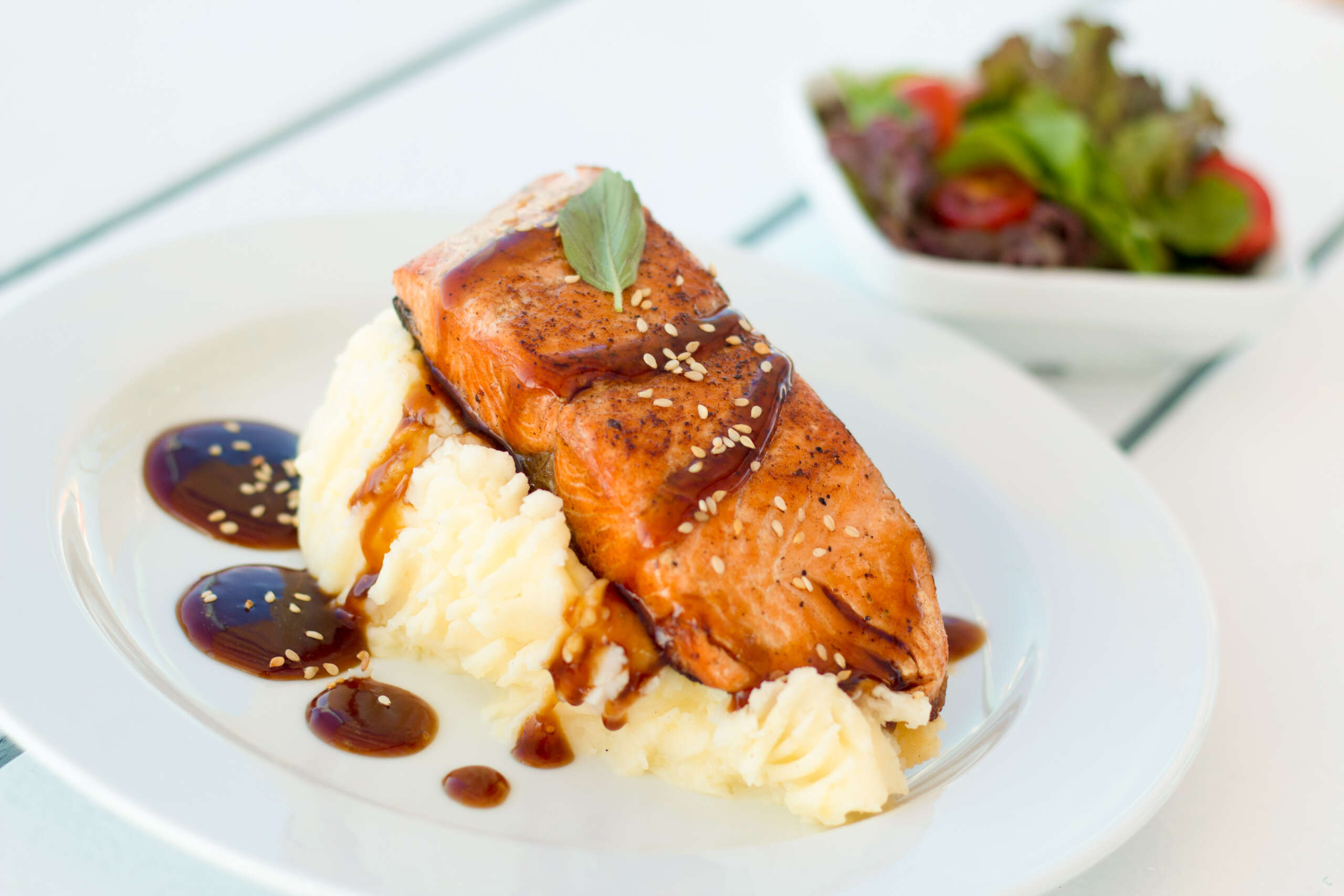 A plate featuring a fresh slice of salmon served alongside creamy mashed potatoes, garnished with herbs for an elegant meal