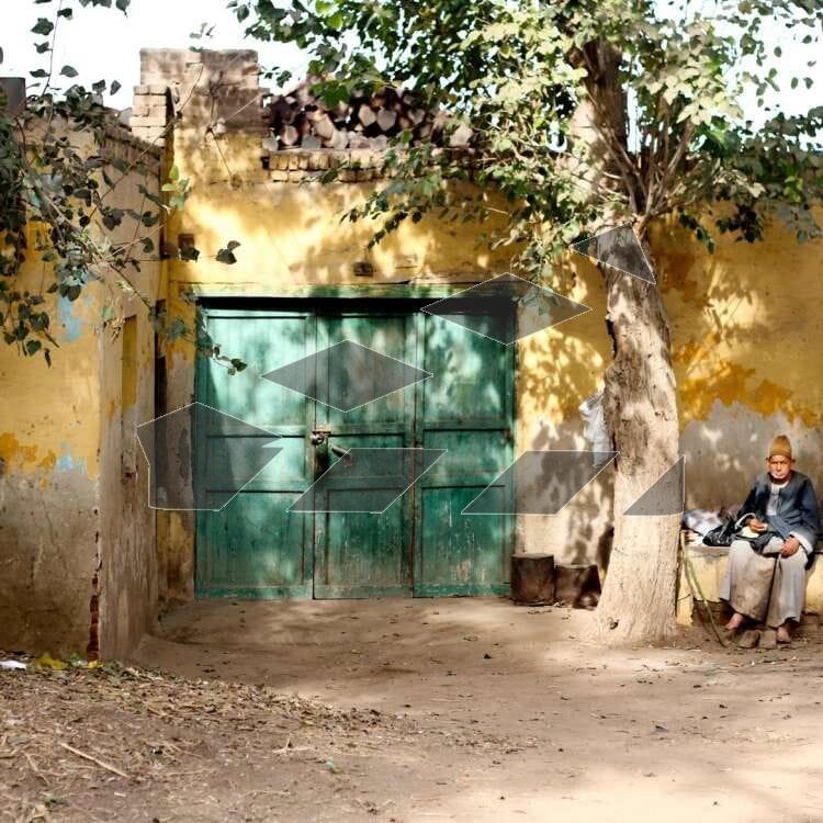 An elderly man sits on a bench outside a traditional building with a green door of Tanta, Egypt