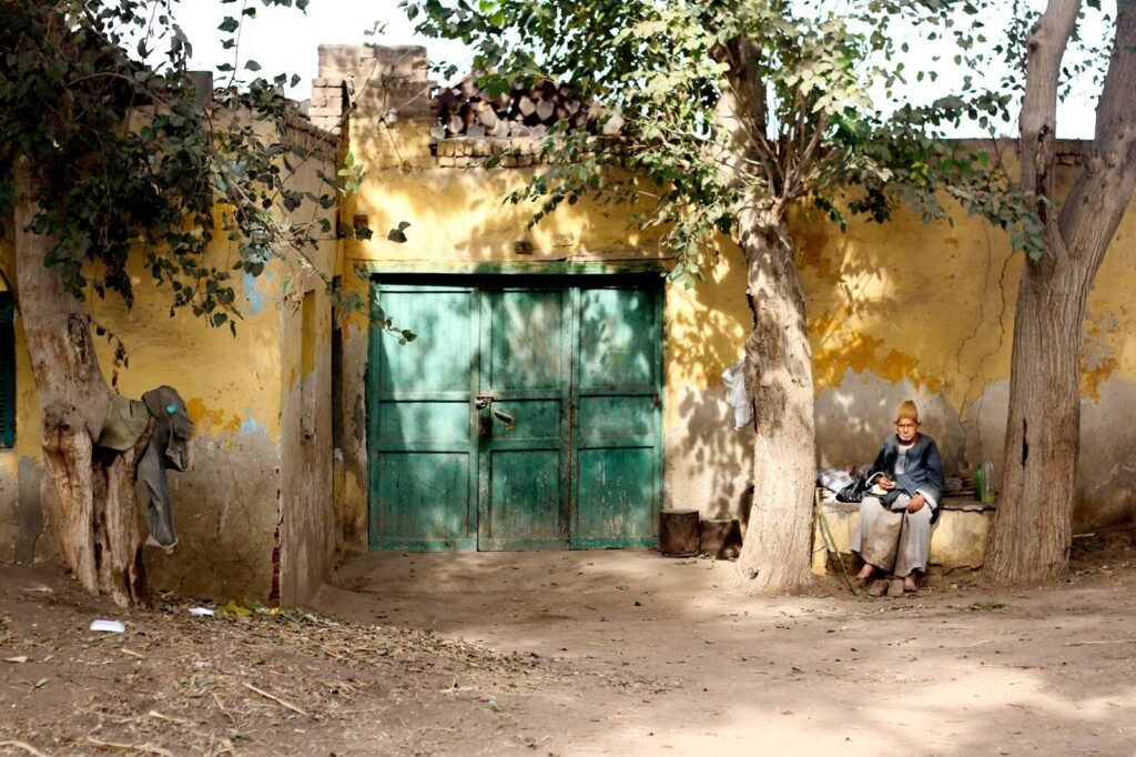An elderly man sits on a bench outside a traditional building with a green door of Tanta, Egypt