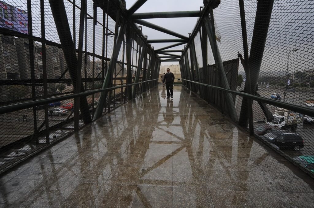 Man Walking on Rainy Pedestrian Bridge in Cairo