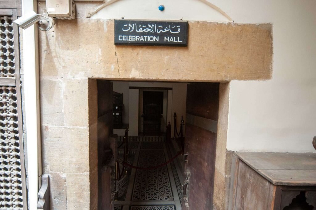 Exterior view of a traditional wooden door at the Gayer-Anderson Museum in Old Cairo, Egypt, with a sign above it reading ‘Banquet Hall’ in Arabic.