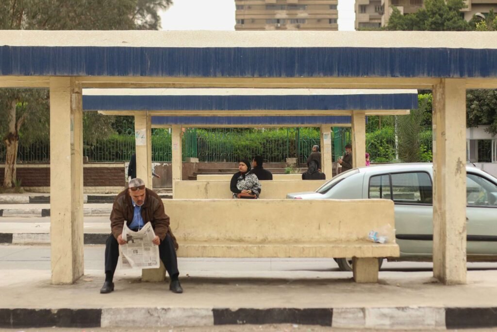 Man Sitting and Reading a Newspaper While Waiting for the Bus in Abbassia, Cairo