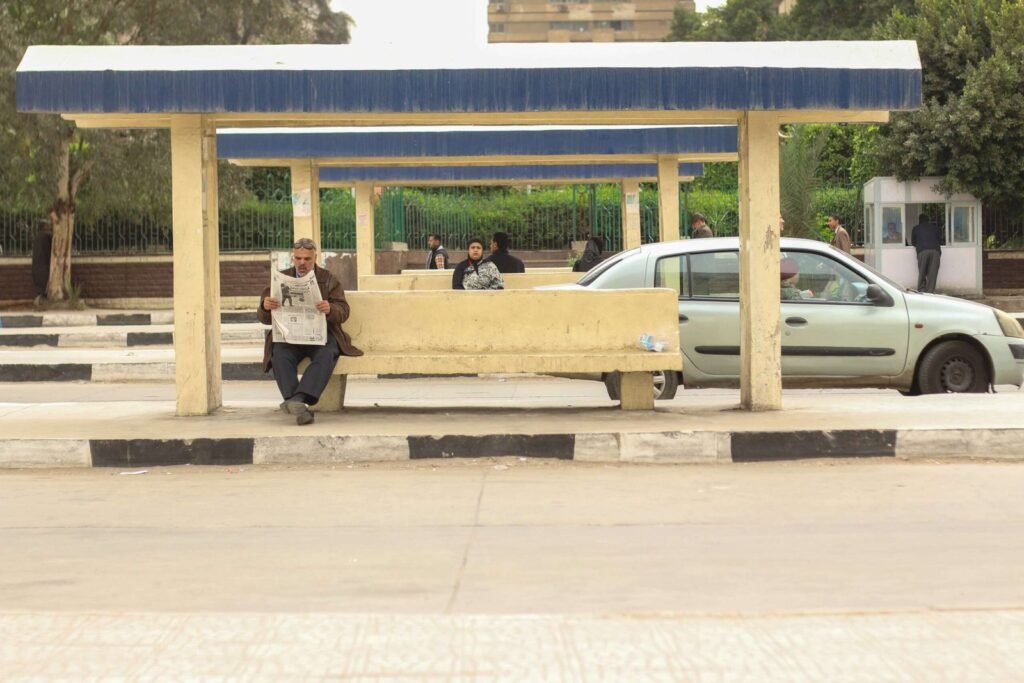 Man Sitting and Reading a Newspaper While Waiting for the Bus in Abbassia, Cairo 2