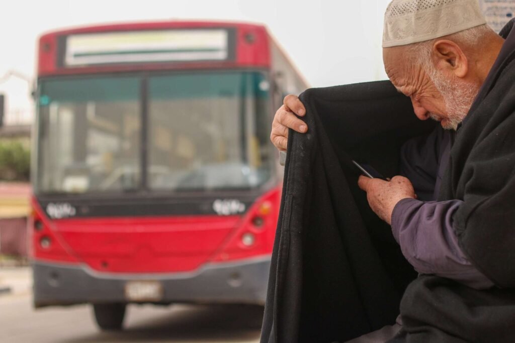 Elderly Man Sitting at Cairo Bus Stop Using Phone