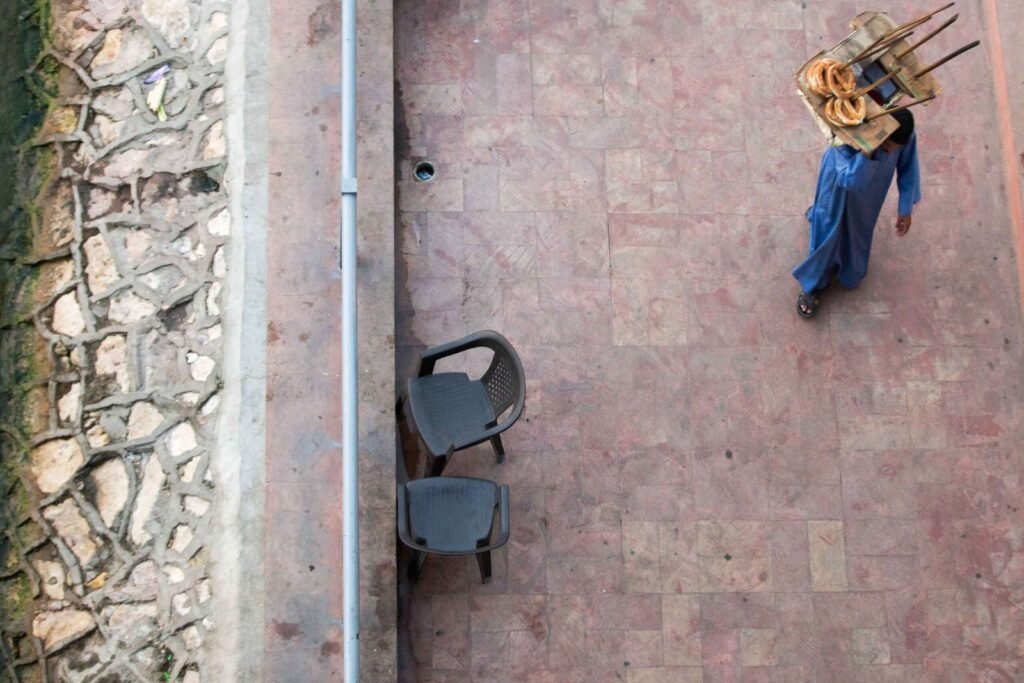 A street vendor in traditional blue attire walks along a tiled sidewalk in Egypt.